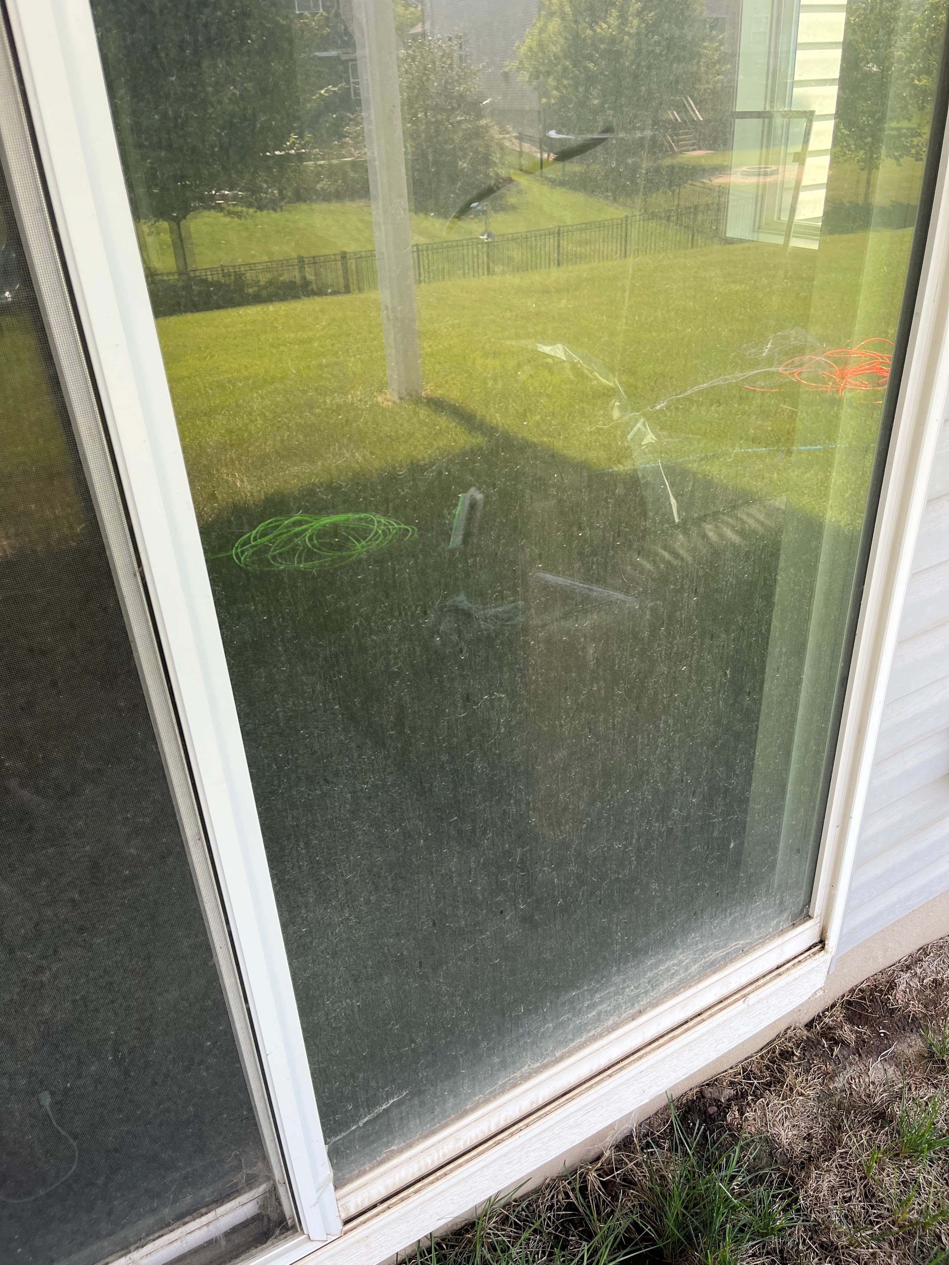 Dirty window reflecting grass and outdoor tools, with visible smudges and streaks.