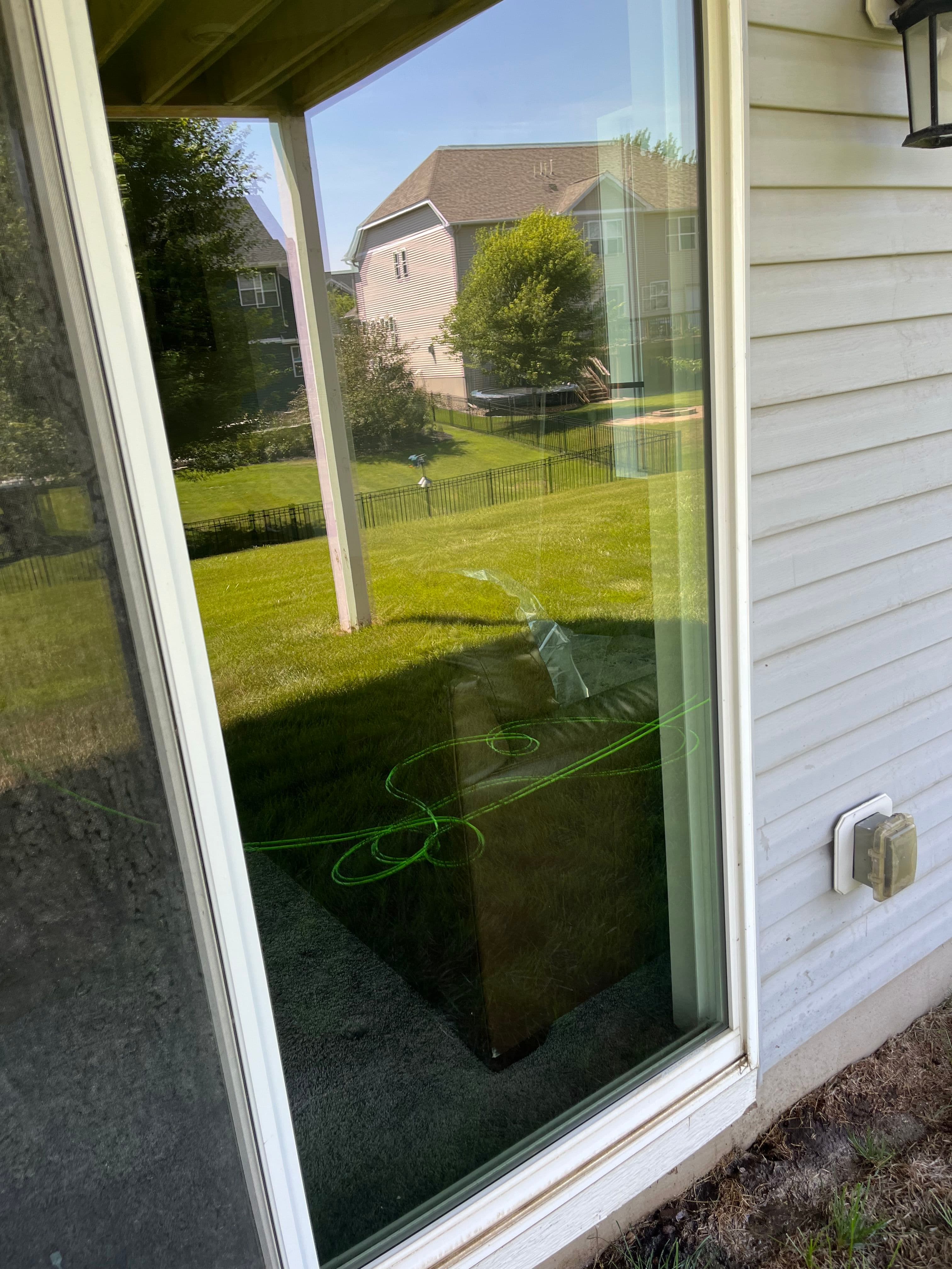Reflection of a lawn and house in a window with green gardening hose nearby.