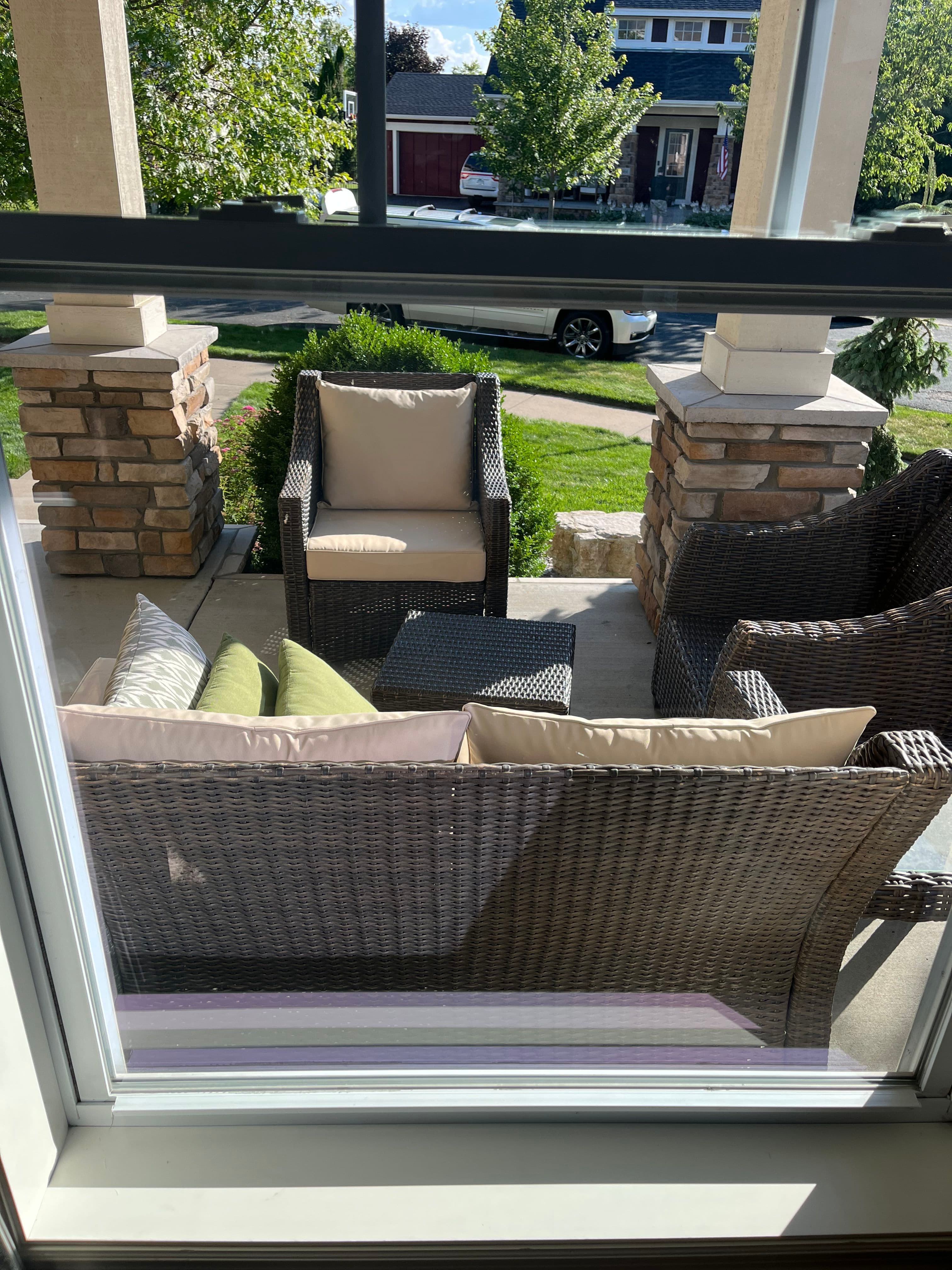 Cozy outdoor seating area with wicker chairs and cushions, viewed from inside a house.