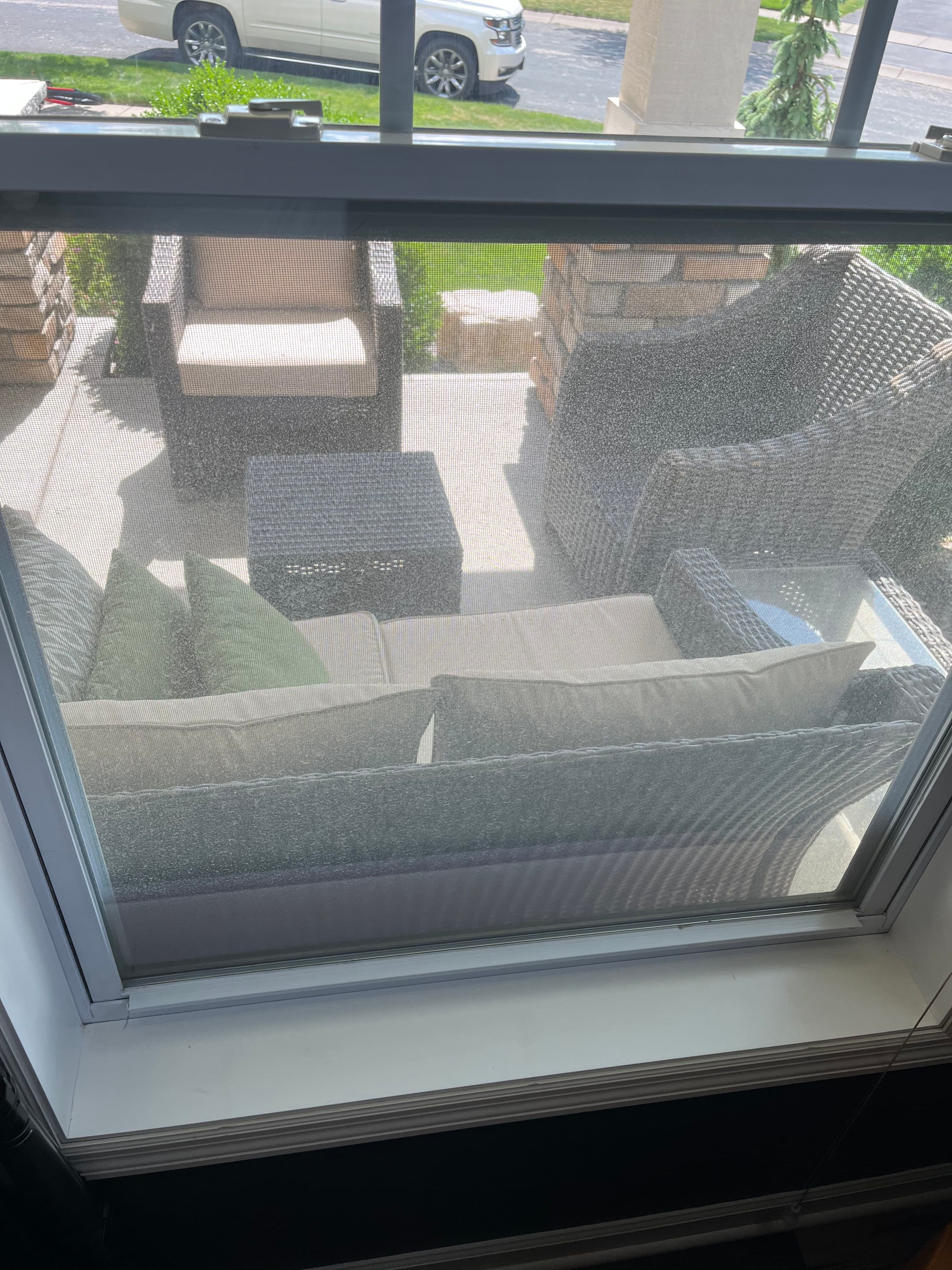 View of an outdoor seating area with wicker furniture and a small table, seen through a window.