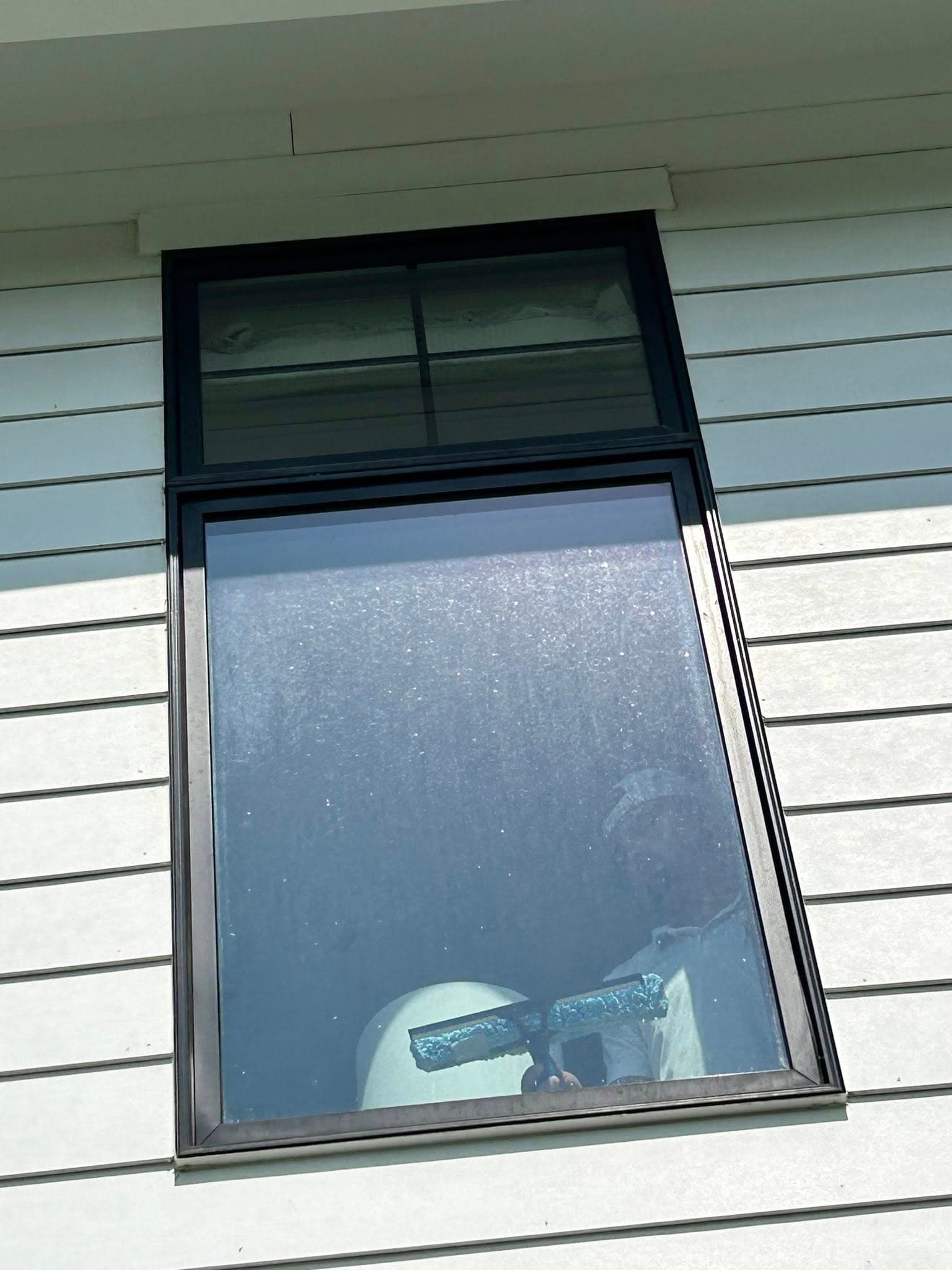 Person cleaning a window with a squeegee on a house exterior, bright sunlight visible.