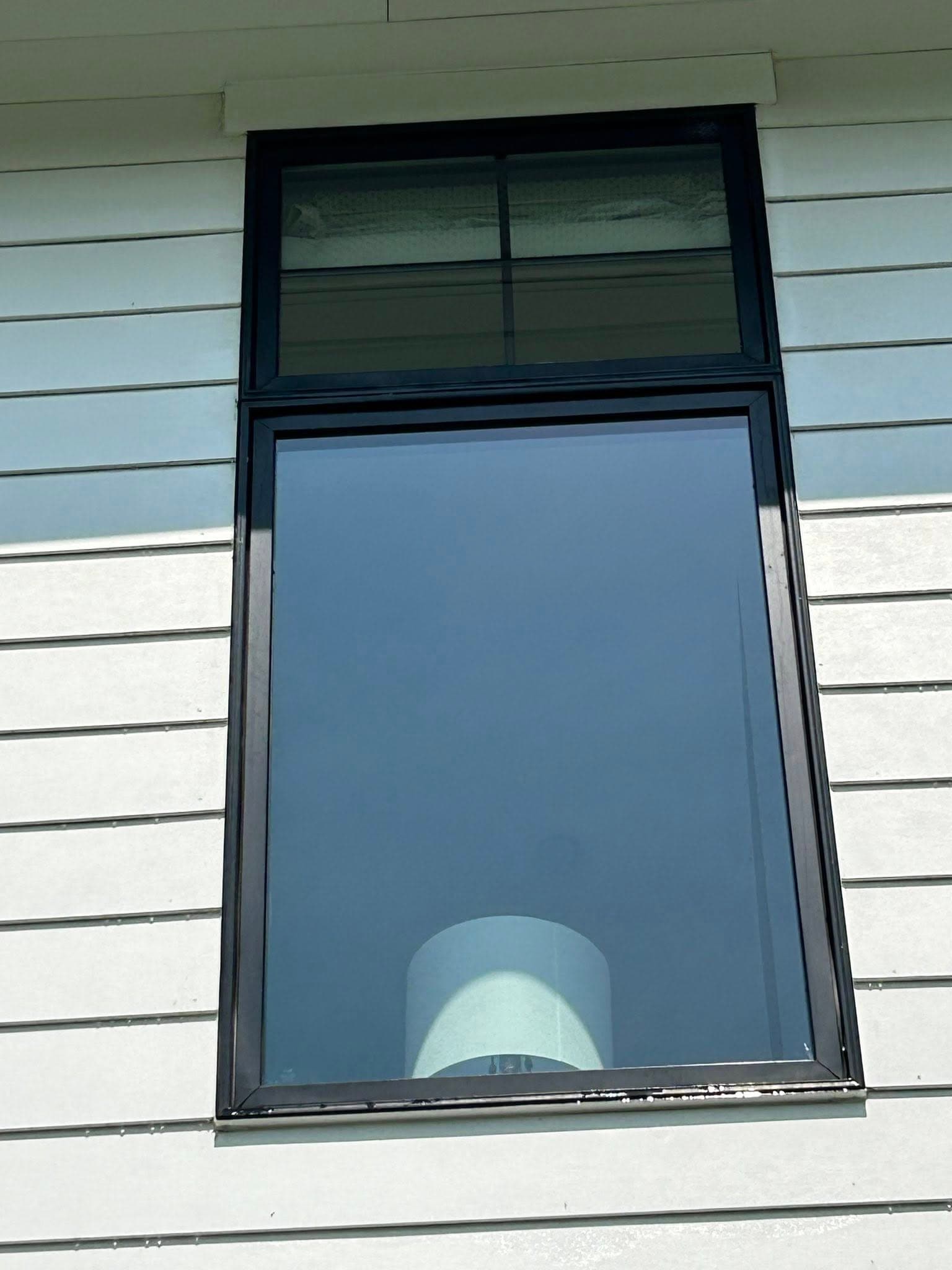 Modern black-framed window showcasing a sleek lamp inside a white-walled building.