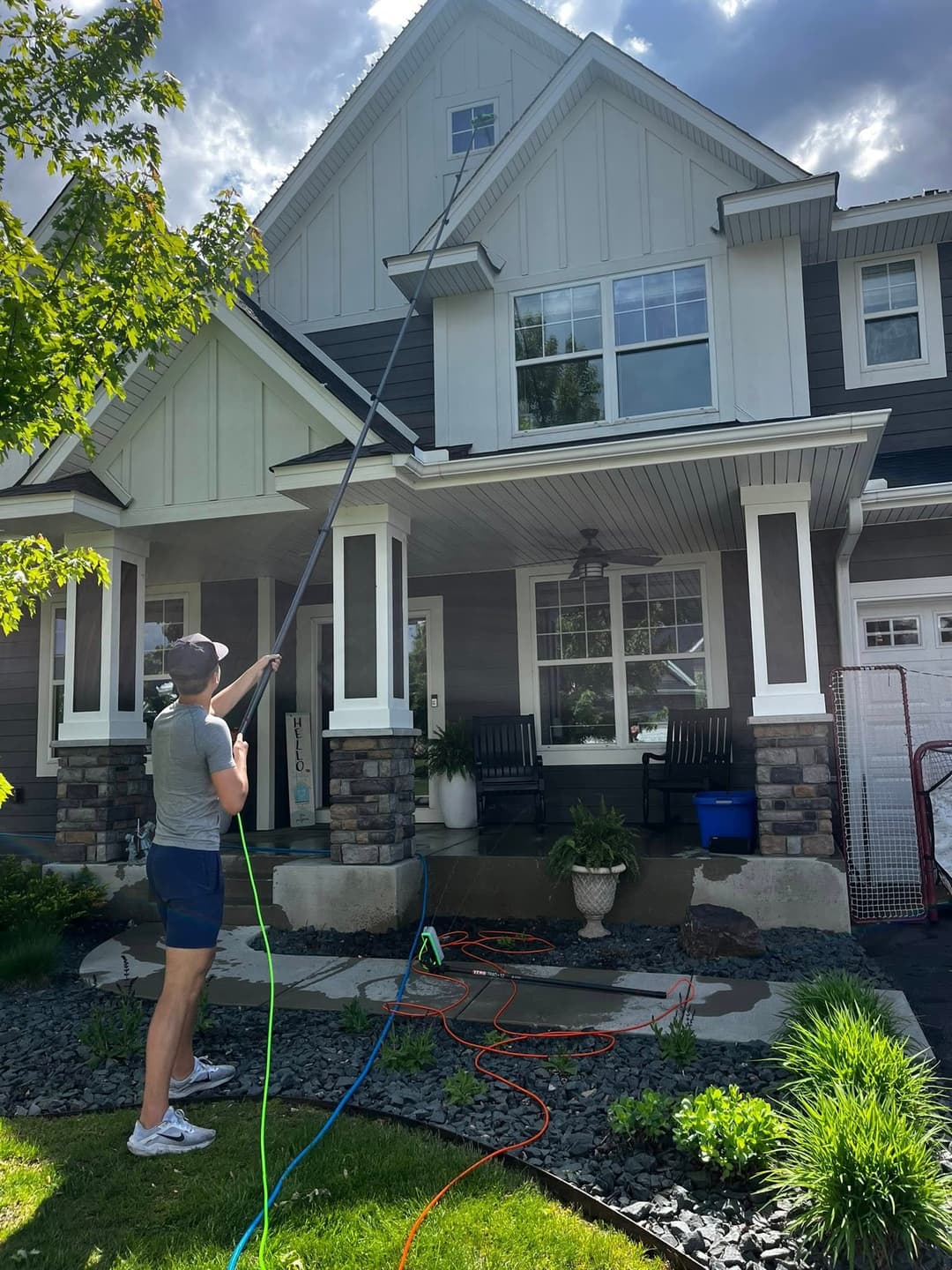 Person using a power washer to clean the exterior of a house on a sunny day.