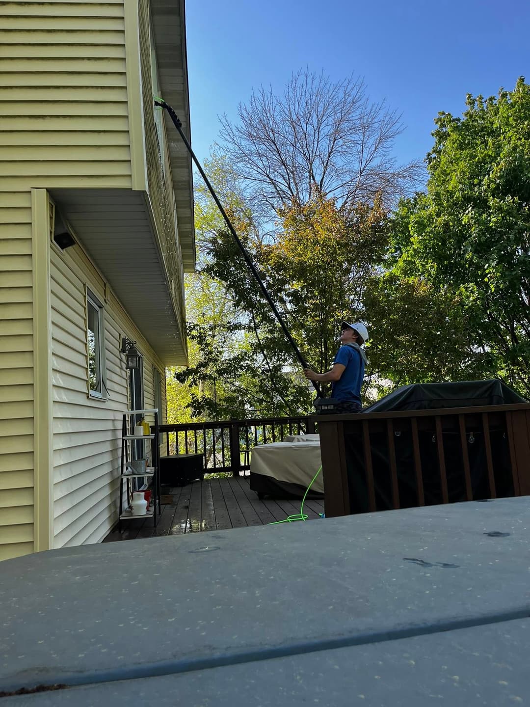 Person using a long pole to clean the exterior of a house on a sunny day.