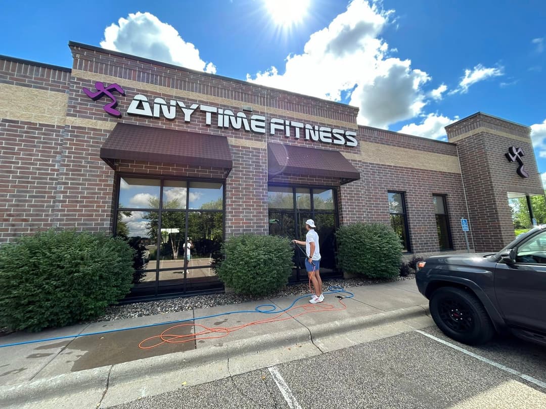 Exterior of Anytime Fitness gym with a worker cleaning windows on a sunny day.