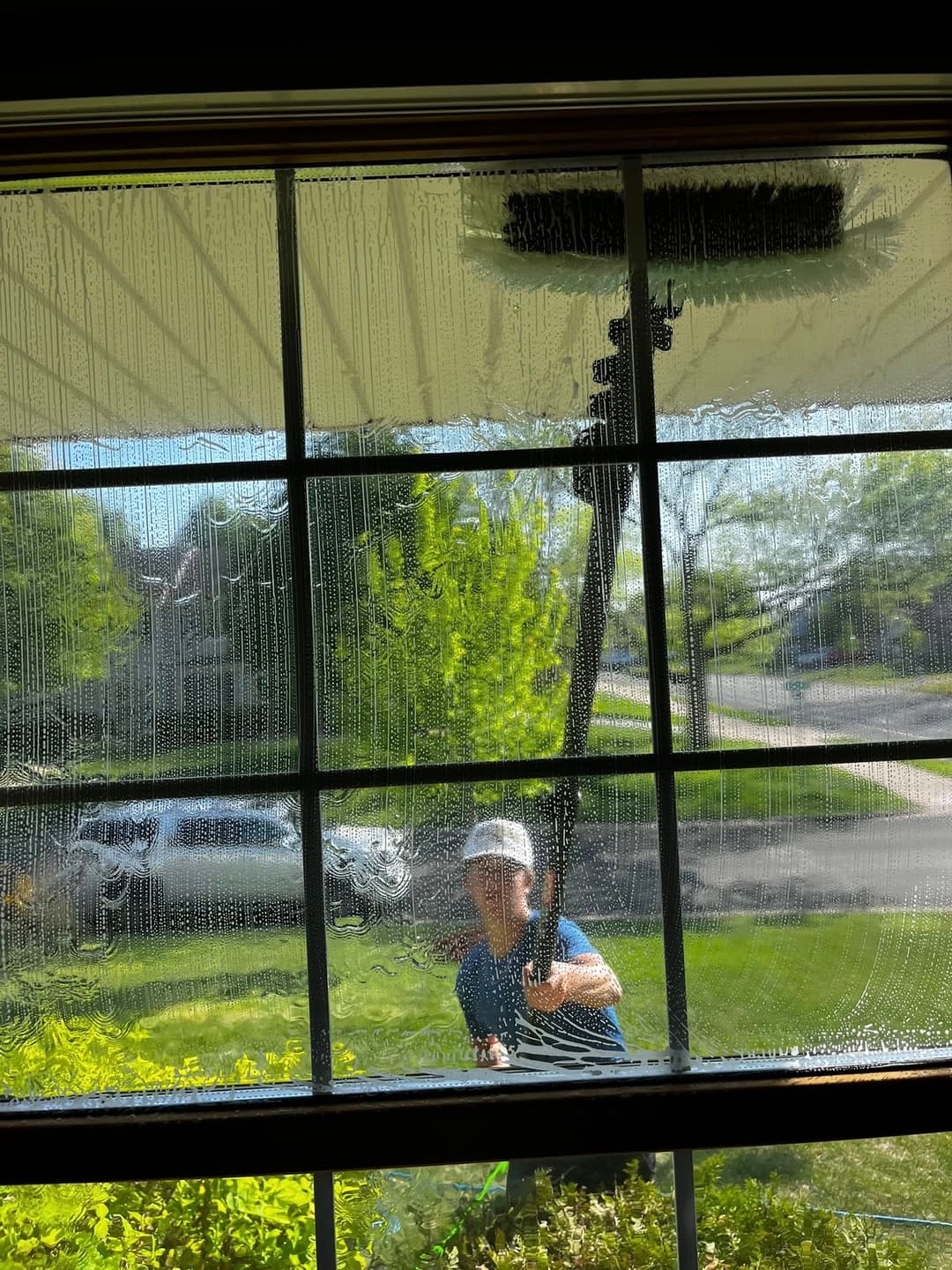 Person cleaning a large window from outside with a squeegee on a sunny day.