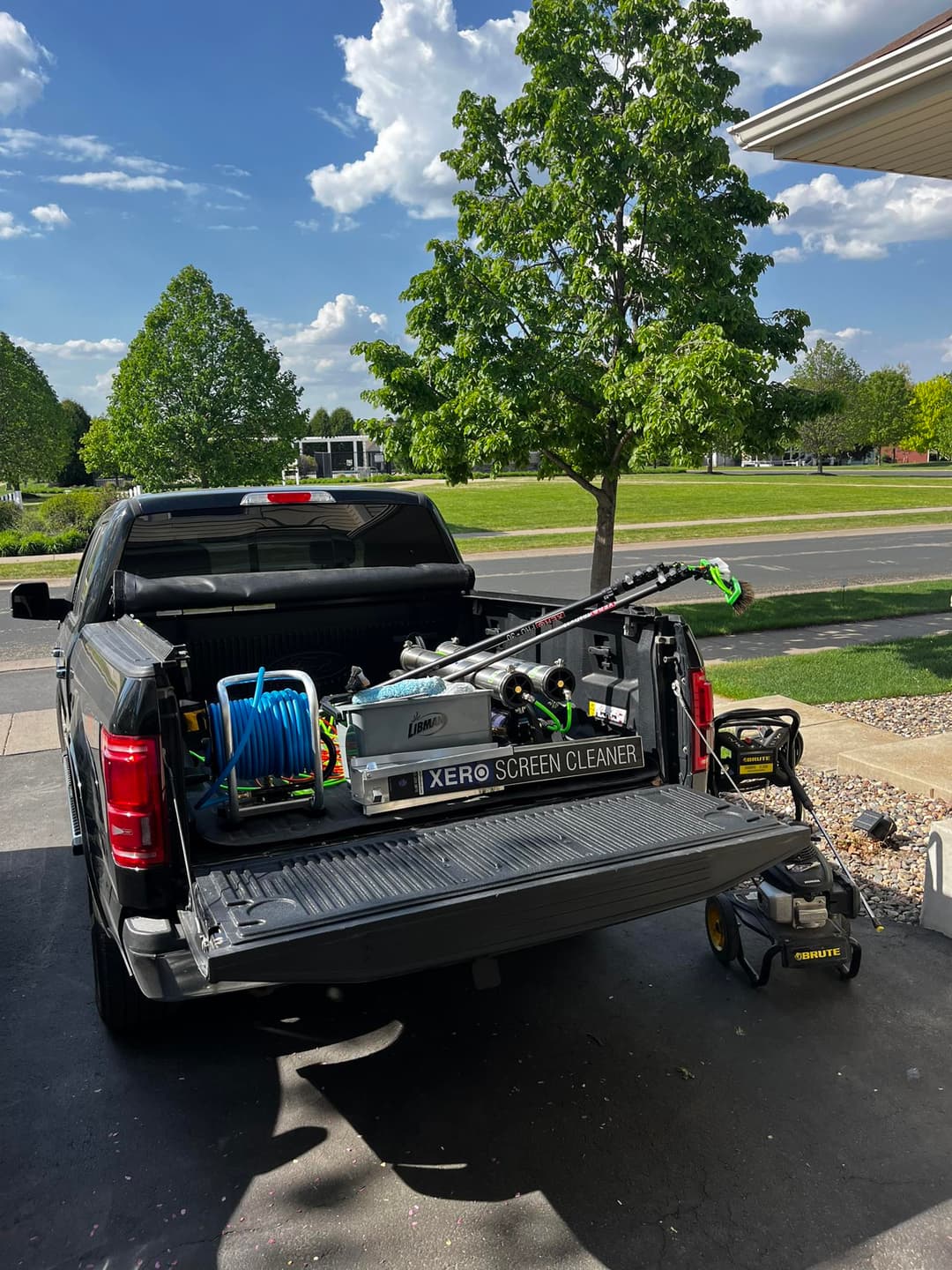 Black pickup truck with cleaning equipment and tools in the bed, parked on a sunny day.